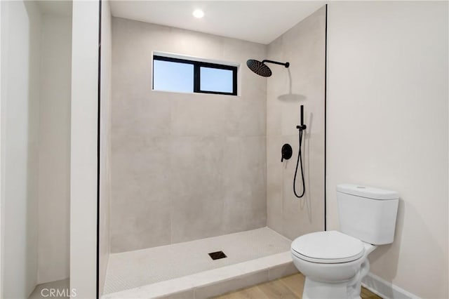 bathroom featuring a tile shower, wood-type flooring, and toilet