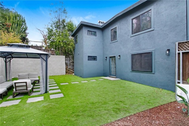 rear view of property featuring a gazebo, an outdoor hangout area, and a lawn