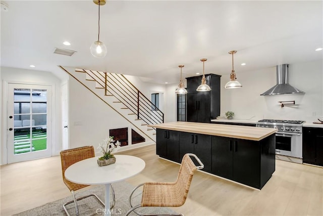 kitchen with decorative light fixtures, a center island, stainless steel stove, light hardwood / wood-style floors, and wall chimney range hood