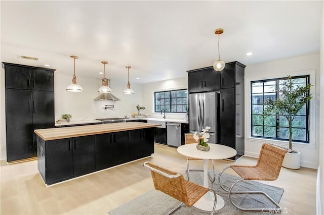 kitchen featuring hanging light fixtures, a wealth of natural light, a kitchen island, and appliances with stainless steel finishes