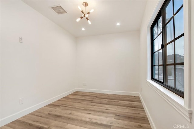 spare room with a notable chandelier and light wood-type flooring