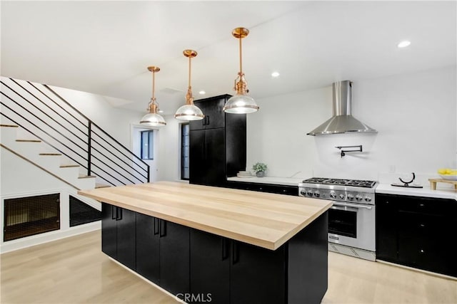 kitchen featuring wall chimney range hood, high end stainless steel range oven, a center island, light hardwood / wood-style floors, and decorative light fixtures