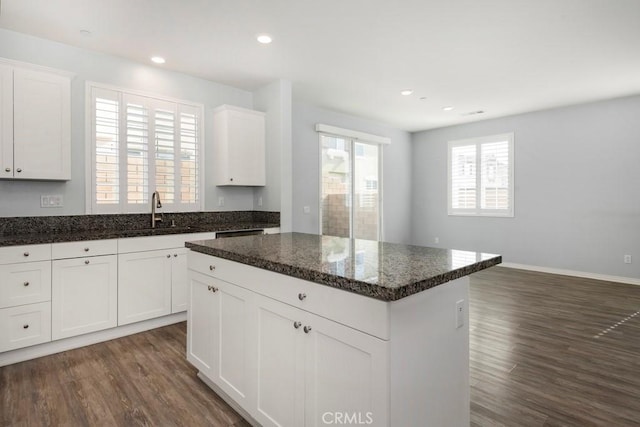 kitchen with dark wood-type flooring, sink, white cabinetry, a center island, and dark stone countertops