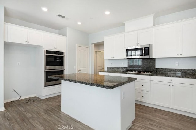 kitchen with white cabinetry, stainless steel appliances, a kitchen island, and dark stone countertops