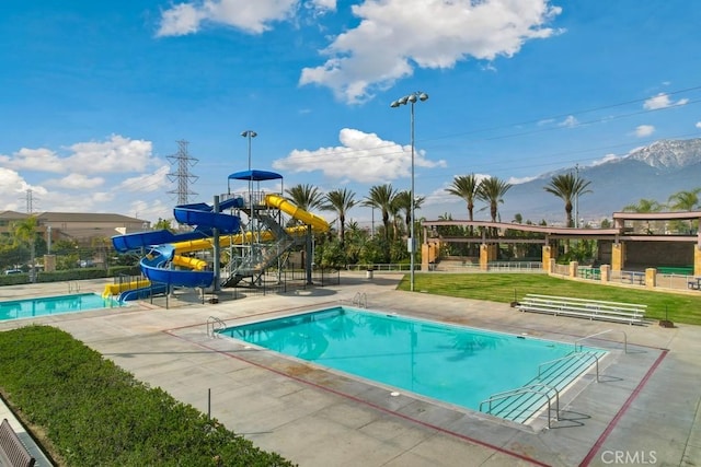 view of pool with a playground, a water slide, and a mountain view