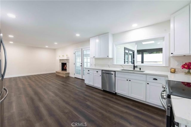 kitchen featuring a stone fireplace, sink, appliances with stainless steel finishes, dark hardwood / wood-style flooring, and white cabinets