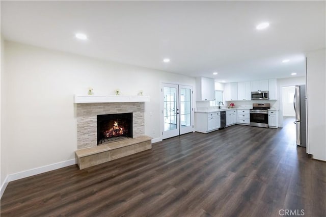 unfurnished living room with dark hardwood / wood-style flooring, sink, a stone fireplace, and french doors