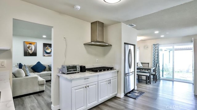 kitchen featuring wall chimney range hood, white cabinetry, stainless steel appliances, light stone countertops, and light wood-type flooring