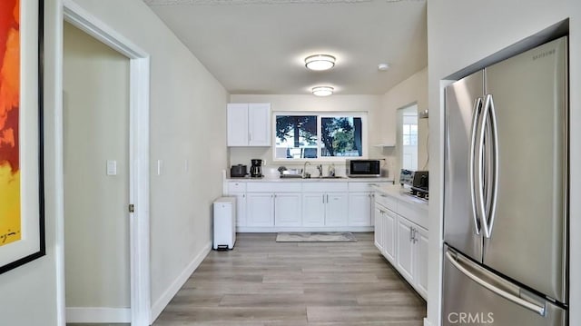 kitchen with sink, white cabinets, stainless steel refrigerator, and light hardwood / wood-style flooring