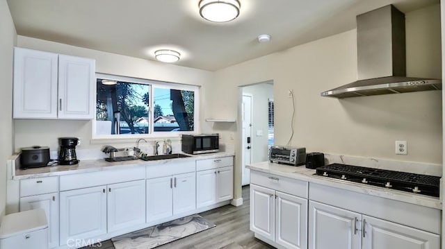 kitchen with a toaster, light wood-style floors, white cabinetry, a sink, and wall chimney exhaust hood