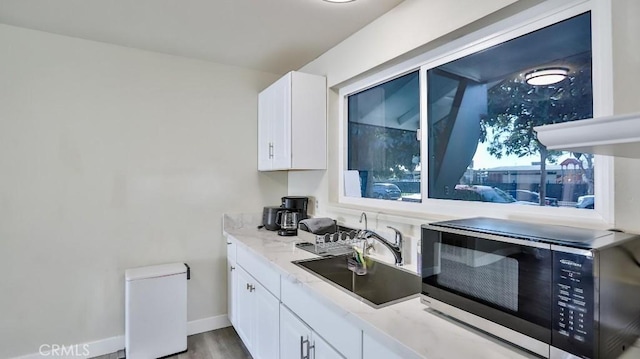 kitchen with white cabinetry, sink, wood-type flooring, and light stone countertops