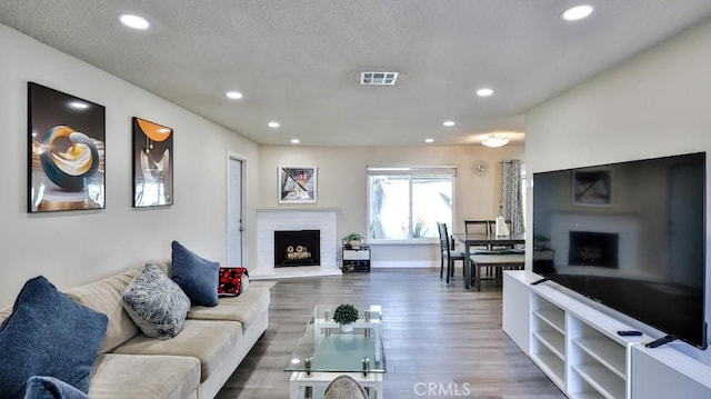 living room featuring a brick fireplace, visible vents, wood finished floors, and recessed lighting