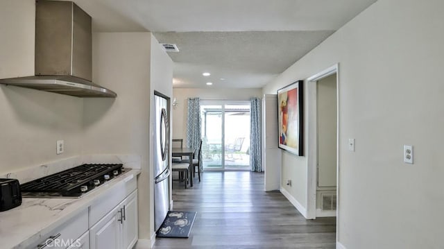 kitchen with dark wood-type flooring, appliances with stainless steel finishes, white cabinetry, light stone counters, and wall chimney exhaust hood