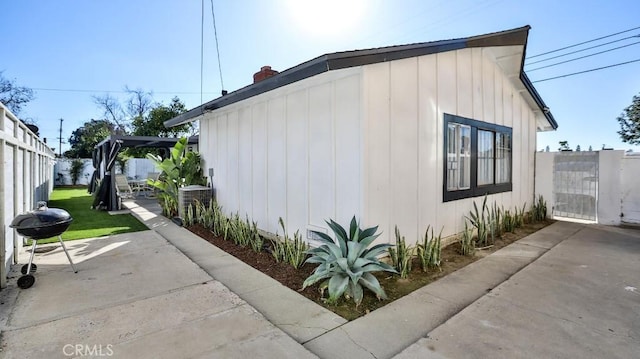 view of side of property with fence, board and batten siding, a gate, a chimney, and a patio area