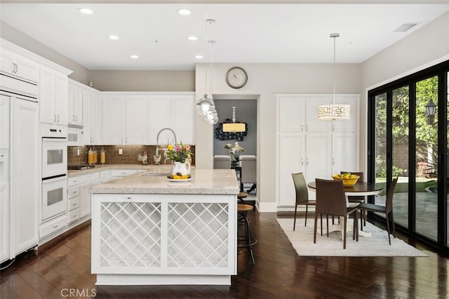 kitchen featuring hanging light fixtures, dark wood-type flooring, white cabinets, and decorative backsplash