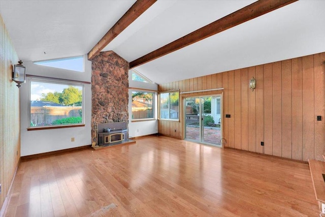 unfurnished living room with wooden walls, lofted ceiling with beams, a wood stove, and light wood-type flooring