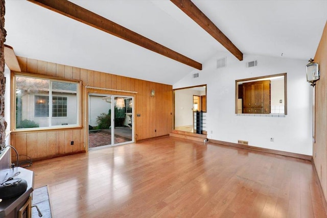 unfurnished living room with vaulted ceiling with beams, a healthy amount of sunlight, light hardwood / wood-style floors, and wood walls