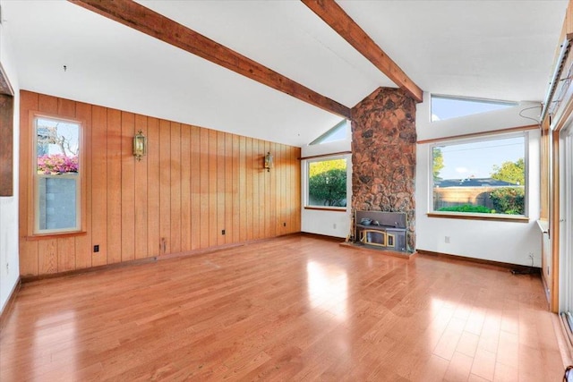 unfurnished living room featuring wood walls, light wood-type flooring, a wood stove, and vaulted ceiling with beams