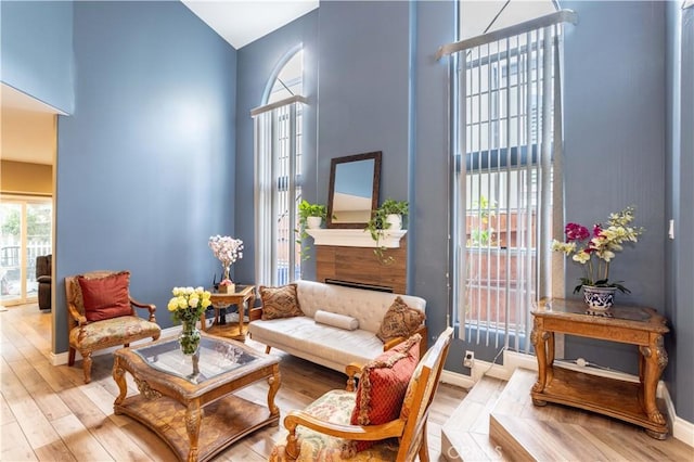 living area featuring a towering ceiling, light wood-style flooring, a fireplace, and baseboards