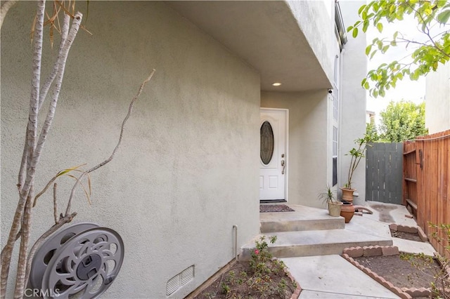 property entrance featuring crawl space, fence, and stucco siding