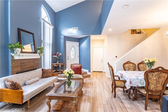 sitting room featuring light wood finished floors, visible vents, baseboards, a towering ceiling, and stairs