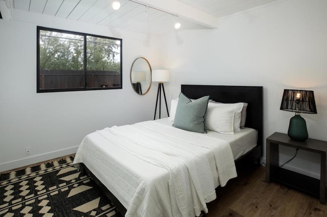 bedroom with beamed ceiling, rail lighting, dark wood-type flooring, and wood ceiling