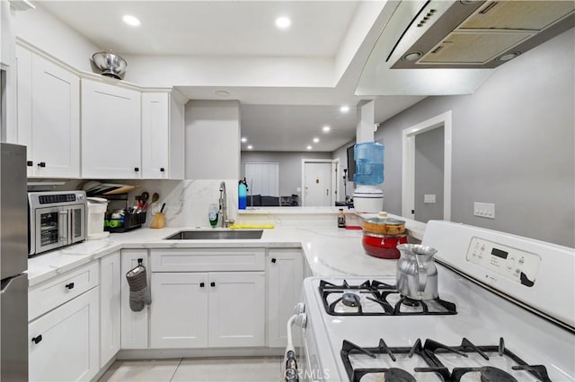 kitchen featuring light stone countertops, white range with gas stovetop, white cabinets, stainless steel refrigerator, and sink