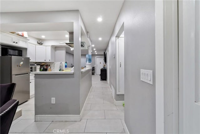 kitchen with light tile patterned floors, white cabinets, kitchen peninsula, stainless steel refrigerator, and tasteful backsplash