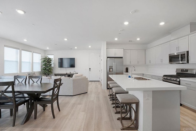 kitchen with sink, a breakfast bar area, backsplash, stainless steel appliances, and a center island with sink