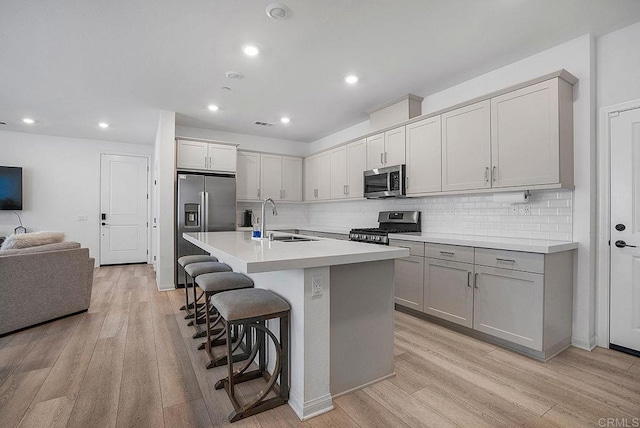 kitchen with appliances with stainless steel finishes, sink, a breakfast bar area, light hardwood / wood-style floors, and a center island with sink