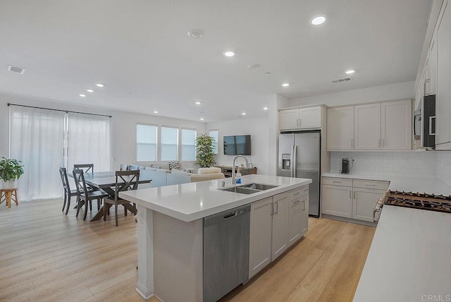 kitchen with sink, a kitchen island with sink, white cabinetry, stainless steel appliances, and light wood-type flooring