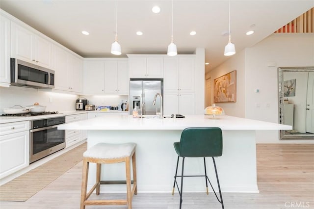 kitchen featuring a kitchen island with sink, pendant lighting, a breakfast bar area, and appliances with stainless steel finishes