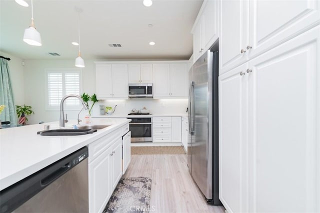 kitchen with sink, appliances with stainless steel finishes, light hardwood / wood-style floors, white cabinets, and decorative light fixtures