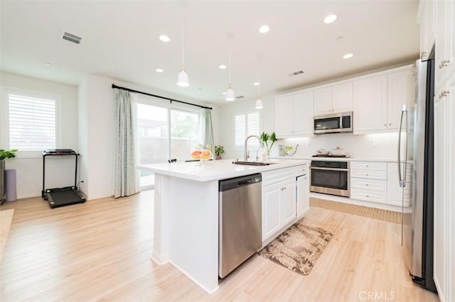 kitchen with sink, appliances with stainless steel finishes, pendant lighting, a kitchen island with sink, and white cabinets