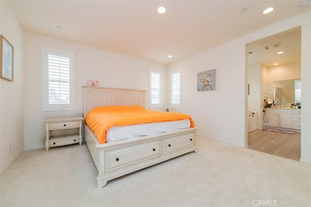 bedroom featuring multiple windows, connected bathroom, and light carpet