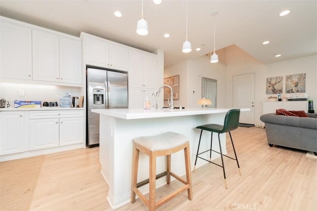 kitchen featuring white cabinetry, stainless steel refrigerator with ice dispenser, a kitchen island with sink, and pendant lighting