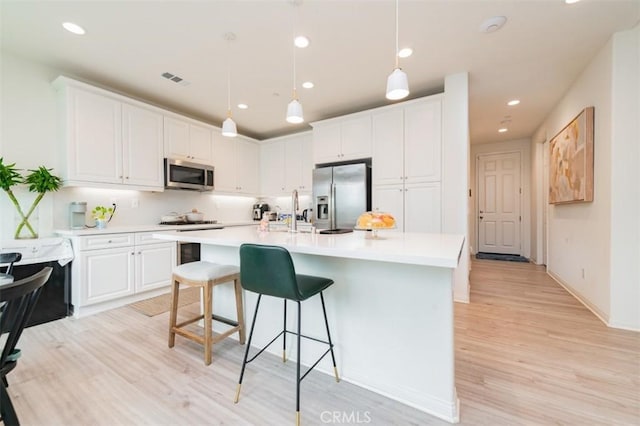 kitchen with decorative light fixtures, an island with sink, white cabinetry, light hardwood / wood-style floors, and stainless steel appliances