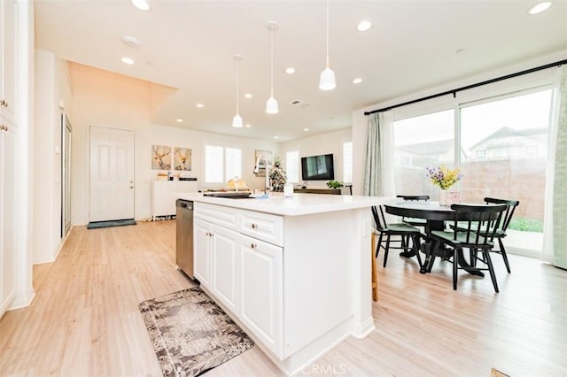 kitchen featuring white cabinetry, a center island, hanging light fixtures, light wood-type flooring, and stainless steel dishwasher