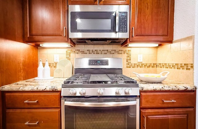 kitchen with light stone countertops, appliances with stainless steel finishes, and backsplash