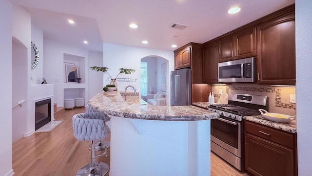 kitchen with appliances with stainless steel finishes, light wood-type flooring, a center island with sink, and a kitchen breakfast bar