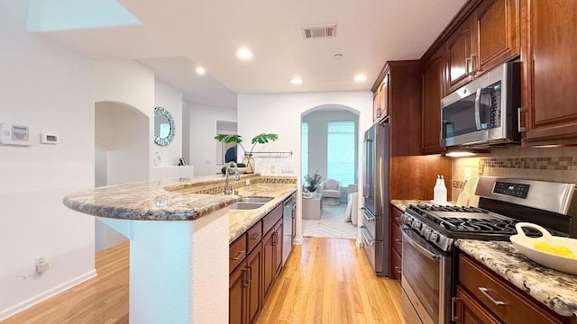 kitchen featuring sink, decorative backsplash, light hardwood / wood-style floors, stainless steel appliances, and light stone countertops