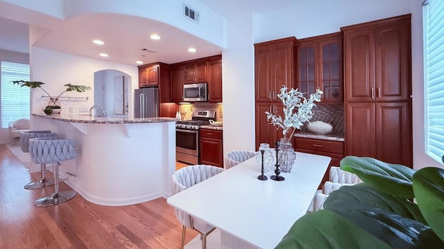 kitchen featuring a breakfast bar, stainless steel appliances, tasteful backsplash, light stone counters, and light hardwood / wood-style floors