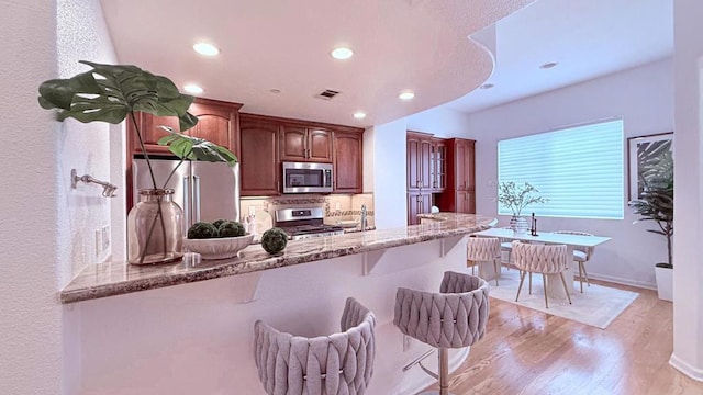 kitchen featuring appliances with stainless steel finishes, dark stone countertops, a kitchen breakfast bar, kitchen peninsula, and light wood-type flooring