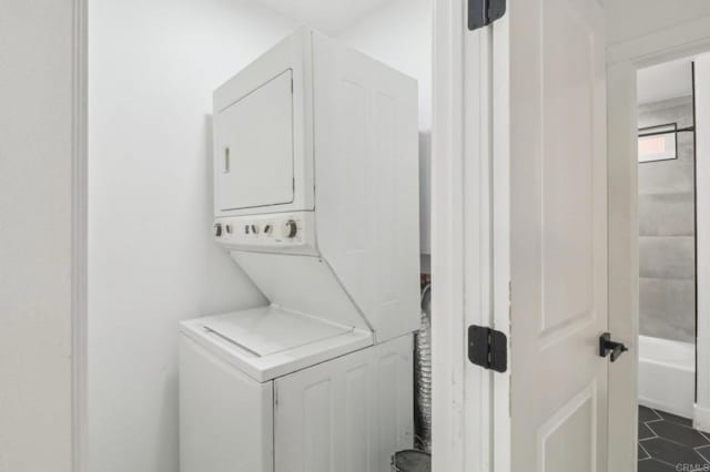 laundry area featuring stacked washing maching and dryer and dark tile patterned flooring