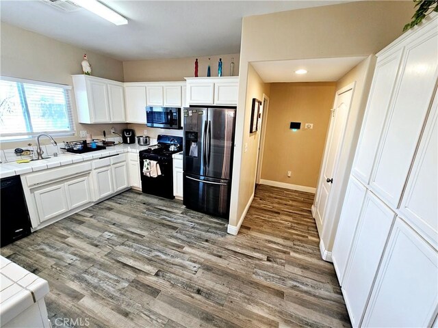 kitchen with sink, white cabinetry, wood-type flooring, black appliances, and tile countertops