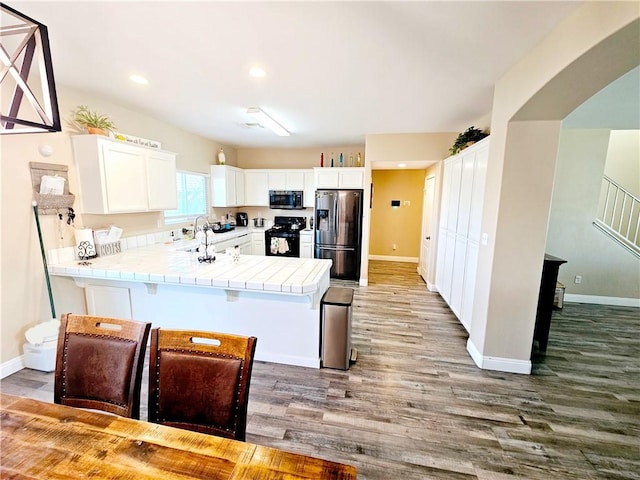 kitchen featuring dark wood-type flooring, a breakfast bar, white cabinetry, stainless steel appliances, and tile counters