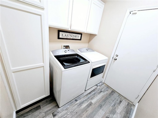 laundry area featuring cabinets, washing machine and dryer, and light hardwood / wood-style flooring