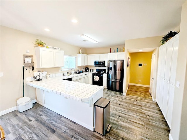 kitchen with white cabinetry, stainless steel appliances, tile counters, light hardwood / wood-style floors, and kitchen peninsula