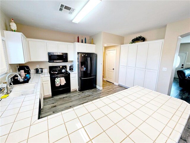 kitchen with sink, tile countertops, black appliances, and white cabinets