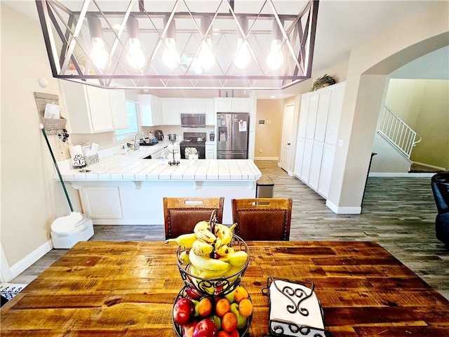 kitchen with stainless steel appliances, tile counters, wood-type flooring, white cabinets, and kitchen peninsula